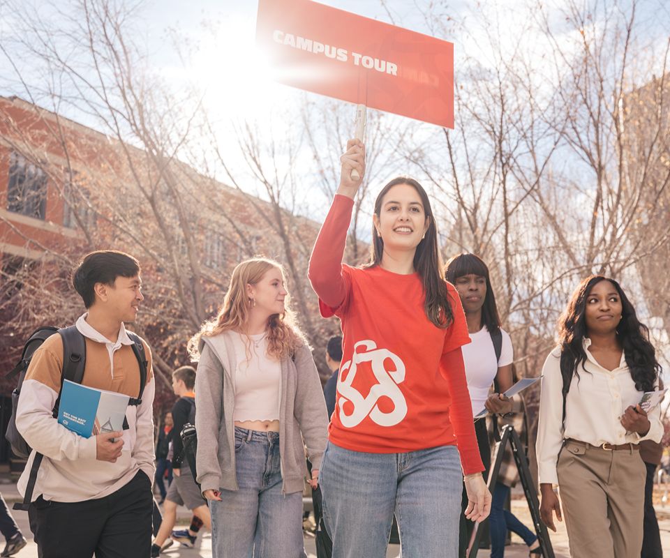 A campus tour guide holds a sign while leading a group of students.