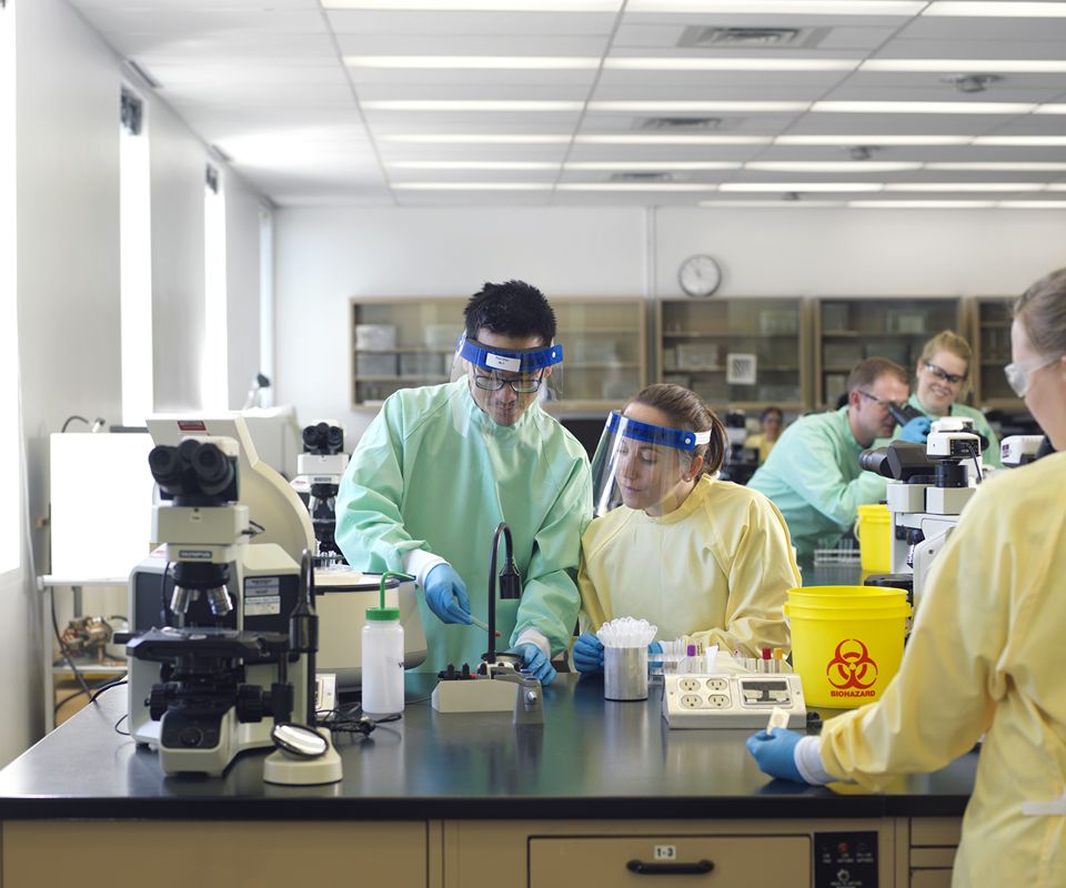 People wearing protective lab gear work together at a laboratory testing equipment.