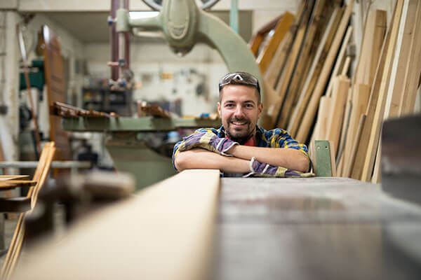A man crosses his arms over planks of wood and smiles at the camera.