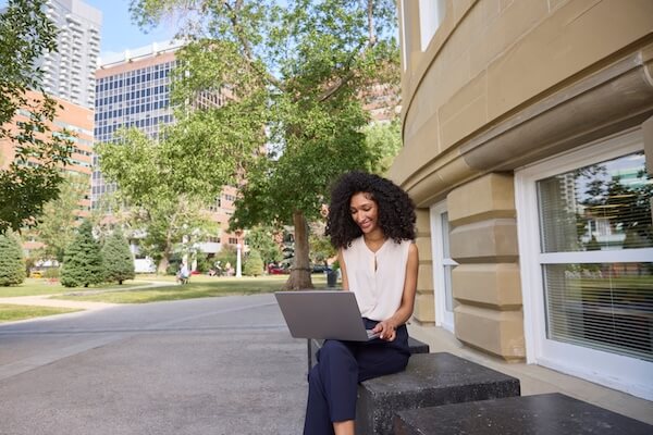 A student sits outside with a laptop