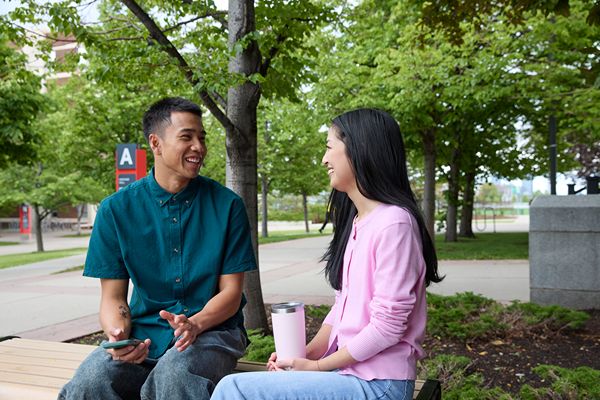 Two people talking while seated outdoors on campus.