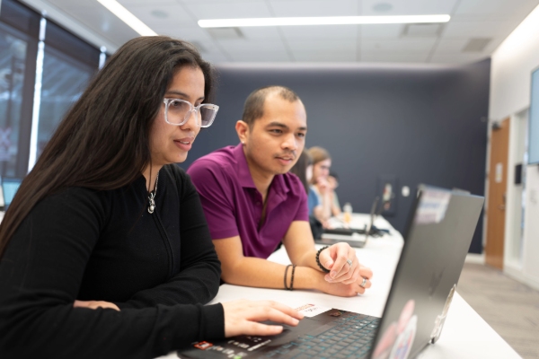 Two students work on a laptop together, focused on the screen.