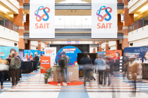 SAIT Open House welcome area in a campus atrium – visitors walking through exhibits and information booths beneath large SAIT banners.