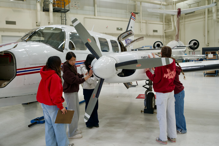 Junior high students stand around a plane and inspect its structure within SAIT's Art Smith Aero Centre.