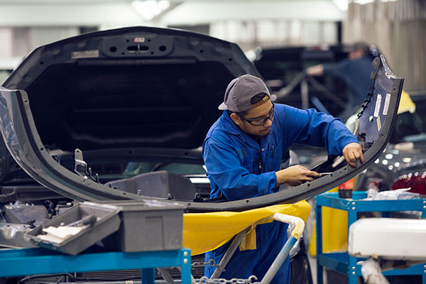 A woman in coveralls works on a car engine.